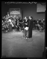 Bing Crosby and Bob Hope standing at microphone before band and telephone operators at telethon for 1952 Olympic Games