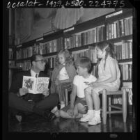 Children's books author, Sid Fleischman sitting on floor of library reading to three children in Santa Monica, Calif., 1964