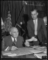 Gov. Frank Merriam exchanging slip of paper with Earl Anderson in his office, Los Angeles, 1935