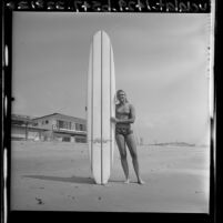 Women's world surfing champion Joyce Hoffman standing with longboard in San Juan Capistrano, Calif., 1964