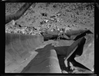 Photographer stands amongst the blast-damaged section of pipe along the Los Angeles Aqueduct in No-Name Canyon, Inyo County vicinity, [about 1927]