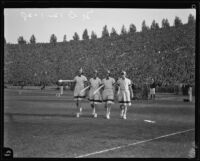 Four armed Trojans march across the Coliseum's field during the USC and Notre Dame football game, Los Angeles, 1928