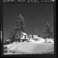 Cottage surrounded by snow covered boulders and trees near Arrowbear, Calif., 1964