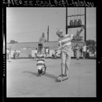 George Trafton doing headstand on skateboard as Danny Bearer watches at skateboarding event in Covina, Calif., 1964