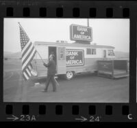 Richard D. Ayers raising flag out front of Bank of America's traveling bank RV in West Covina, Calif., 1967