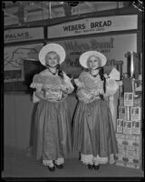 Sylvia and Louise Haines, known as the Weber Gingham Twins, stand in front of the Weber Bread exhibit at the Food and Household Show, Los Angeles, 1933