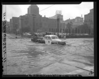 Tow truck pushes stalled taxi across water-filled intersection at 5th and Flower Streets in Los Angeles, Calif., 1948