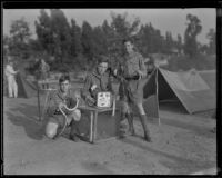 Boy Scouts at a camping event in a park pose with snakes and framed butterflies, circa 1935