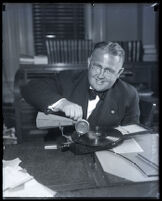 Los Angeles judge Leroy Dawson seated at desk playing with a portable phonograph, Los Angeles, circa 1931