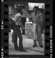 Fusion Energy Foundation advocate, with sign reading "Nuclear Plants Are Built Better Than Jane Fonda," talking to traveler at Los Angeles International Airport, 1980