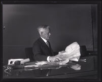 Major Frederick R. Burnham seated at a desk, reading a folded map, Los Angeles, 1926
