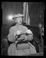 Gossip columnist Hedda Hopper, posing for camera on witness stand during forgery trial in Los Angeles, Calif., 1955