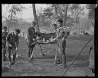 Boy Scouts at a food preparation table at a camping event in a park, circa 1935