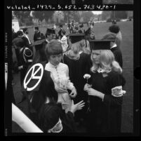 Group of UCLA students at commencement wearing gowns with "peace now" armbands and peace symbol on cap, 1970