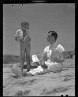 Actor Neil Hamilton and daughter Patricia on beach holding wooden shoes, Malibu, 1937