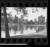 Man fishing in Echo Park lake with buildings of Bunker Hill in background in Los Angeles, Calif., 1975