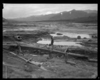 Three men in a vast muddy plain left by the flood following the failure of the Saint Francis Dam, Santa Clara River Valley (Calif.), 1928