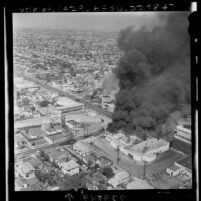 Aerial view of two buildings on fire on Avalon Blvd. between 107th and 108th street during Watts Riots, Los Angeles, 1965