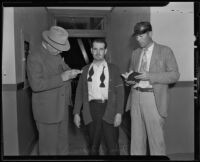 John Moore stands while Detective Lieutenant F. L. McGlinchey reads something to him and another man writes in his notepad, Los Angeles, 1935