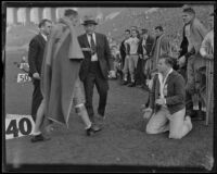 Stub Allison, assistant coach of the Golden Bears, approaches a player draped in a blanket as other players watch in the sideline at the Coliseum, Los Angeles, 1934