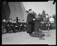 Robert G. Sproul, in cap and gown, speaking at UCLA graduation ceremony at Hollywood Bowl, Los Angeles, [1930s?]