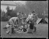 Boy scouts cook over an open fire at a camp in a park, circa 1935