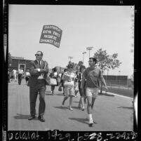 Cal State Los Angeles students, one with "Communist Lies" placard walking to Dorothy Healey speech, 1964