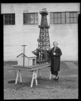 Whittier College co-ed Alma Furman stands beside Elmer Calkins' model oil derrick, Whittier, 1936