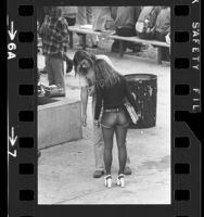 Female student dressed in cut-off jean shorts, tights and platform shoes talking with classmate at Hamilton High School in Los Angeles, Calif., 1973