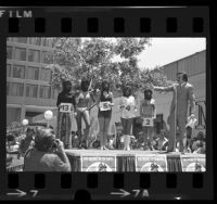 Gary Owens onstage with contestants in ape masks during Most Beautiful Ape contest in Century City, Calif., 1972