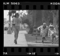 Man with walkman jogging past elderly couple seated on park bench in Santa Monica, Calif., 1981