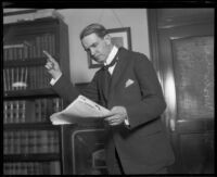 Distric Attorney Thomas Lee Woolwine reads papers with finger pointed in gesture, Los Angeles, 1920-1923