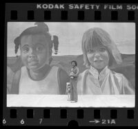 Muralist Richard Wyatt standing before his "Inner City Relief" mural in Los Angeles, Calif., 1982