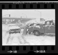 People pushing stalled truck off Magic Mountain Parkway during snow storm in Valencia, Calif., 1974