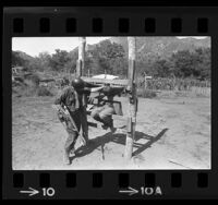 Soldier in wooden stocks at simulated Viet Cong POW camp at Camp Pendleton, Calif., 1966