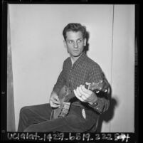 Folk musician Mike Seeger seated in chair playing banjo, Calif., 1964