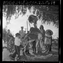 Nursery school students and teachers dressed in kimonos and Mexican costumes hitting pinata in Los Angeles, Calif., 1965