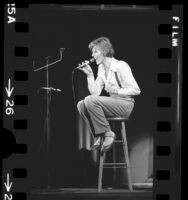 David Bowie, seated on stool during performance at the Universal Amphitheater in Los Angeles, Calif., 1974