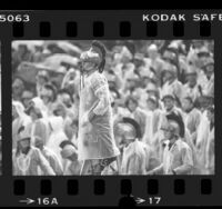 USC Trojan Marching Band leader in uniform and raincoat, standing above raincoat clad band during game in Los Angeles, Calif., 1984