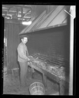 Chinese man standing at community kitchen grill in vegetable market in Los Angeles, Calif., 1934