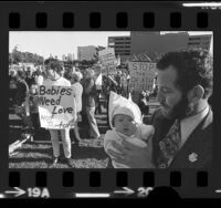 Man holding baby amongst Pro-life demonstrators with signs, one reading "Babies Need Love Not Torture" in Los Angeles, Calif., 1974