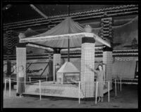 Two women stand, holding oranges, in front of Riverside's display at the National Orange Show, San Bernardino, 1934