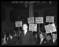 Attorney Gregory Creutz speaking before Board of Supervisors as people behind him hold up signs protesting oil drilling in Los Angeles, Calif., 1947