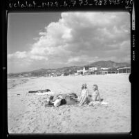 Three people sunbathing on the shoreline of The Malibu Colony, Calif., 1976