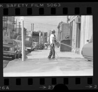 Man hosing down sidewalk on Towne Avenue in violation of water conservation ordinance in Los Angeles, Calif., 1977