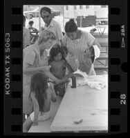 Nurse Janice Estes attending to toddler with sores at "Dust Bowl Hilton," homeless camp in Los Angeles, Calif., 1987