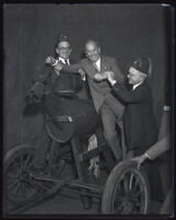 Judge Guy F. Bush and another man wearing a fez, holding a man over a wooden horse, Los Angeles, 1920s