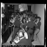 Two police officers holding back a group of Sonny and Cher fans at Los Angeles International Airport, 1965