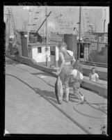 Daughters of fisherman walk down dock with signs on back protesting price cut by canneries on Terminal Island, Calif., 1960