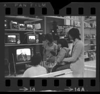 Women with children watching Senate Watergate Hearings on televisions in a Sears department store in Los Angeles, Calif., 1973